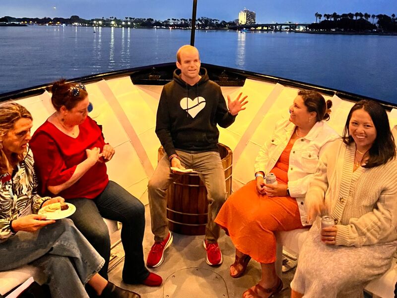 Hansen facilitating a small circle at the bow of a boat at dusk under string lights