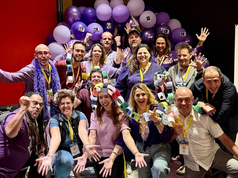 Connection Crew team celebrating with attendees in front of a wall of purple balloons at a conference