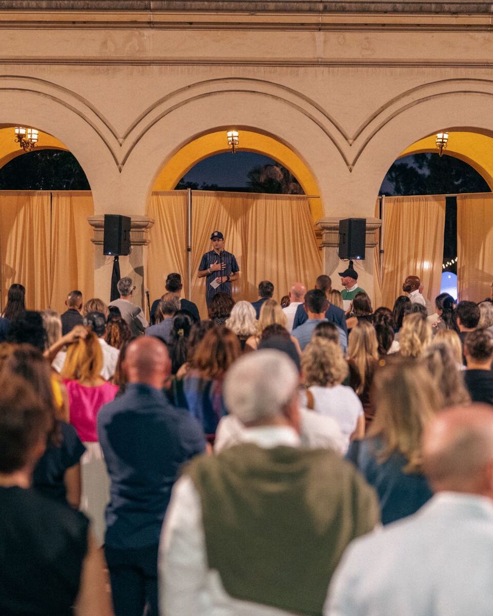 Hansen speaking to a crowd beneath the lit arches of Balboa Park at the Balboa Park Table